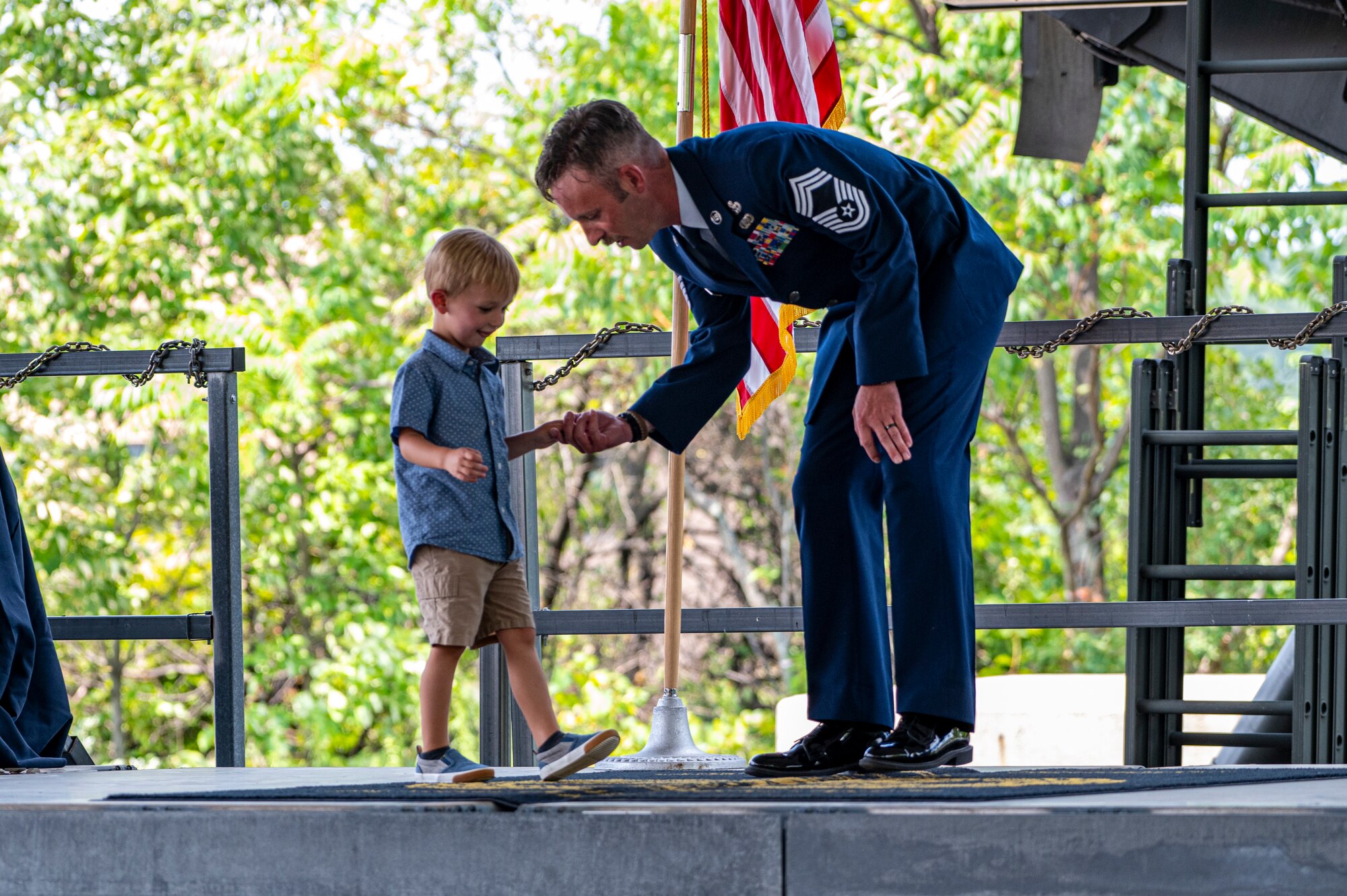 CMSgt O'Bryan kneels right of frame facing toward his son, hand in hand, as his son walks toward him on stage