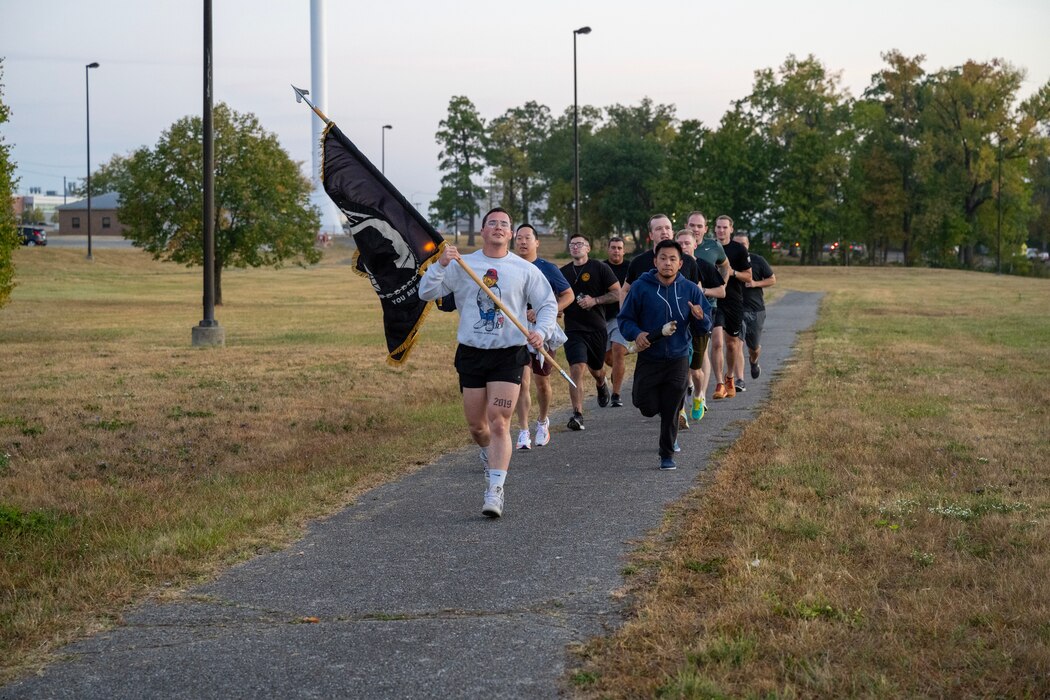 Individuals running on a path while holding a POW/MIA flag.