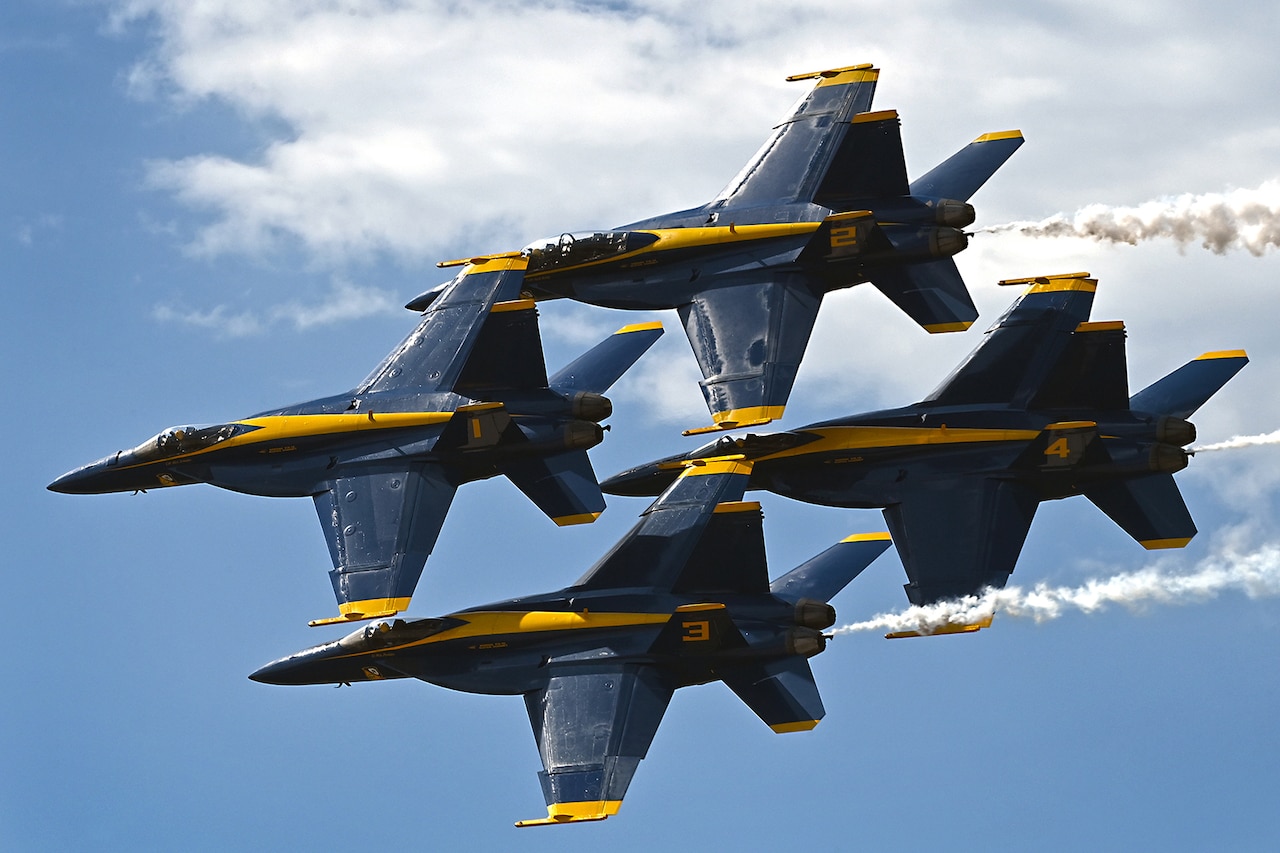 Four military aircraft fly in close formation against a cloudy blue sky.
