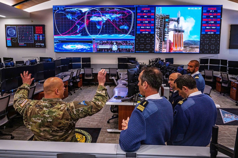 U.S. and foreign service members in uniform stand on a watch floor.