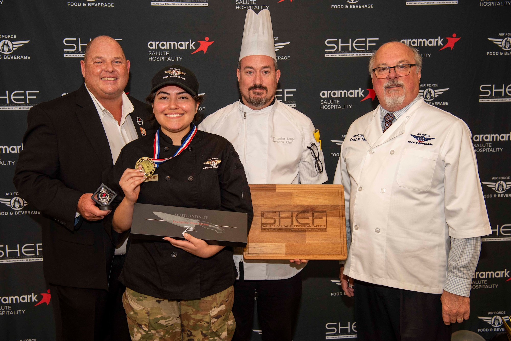 Group of four with winning Airman holding a medal and chef knife while her executive chef holds a SHEF emblazed cutting board