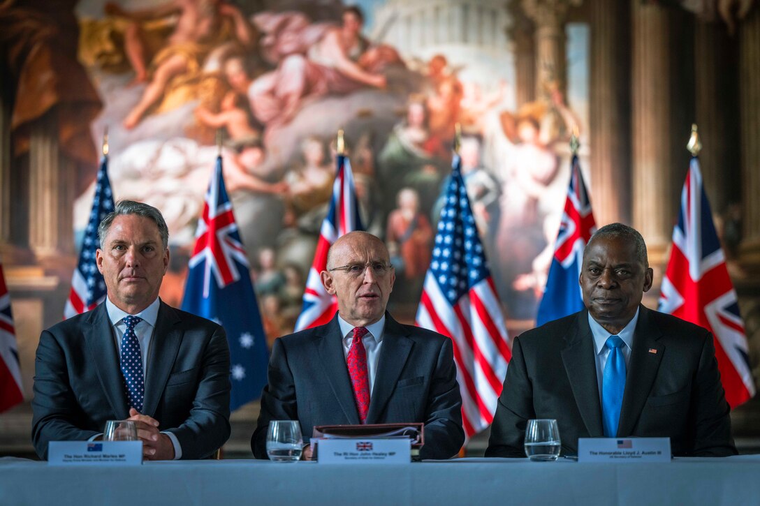 Three civilians sit next to each other at a long table.
