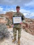 U.S. Army Soldier in uniform poses with a certificate in the desert