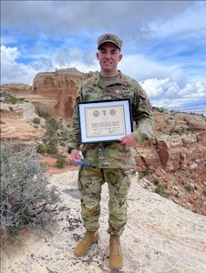 U.S. Army Soldier in uniform poses with a certificate in the desert