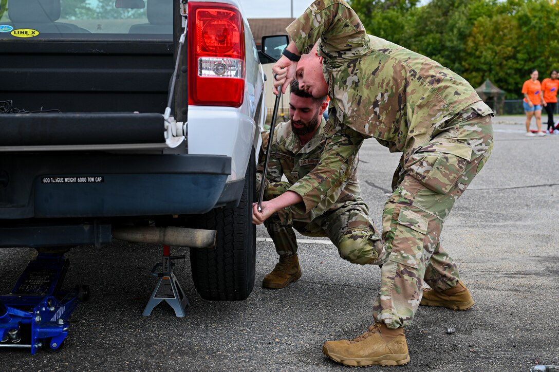 Two Airmen in uniform work together to tighten screws on a tire.
