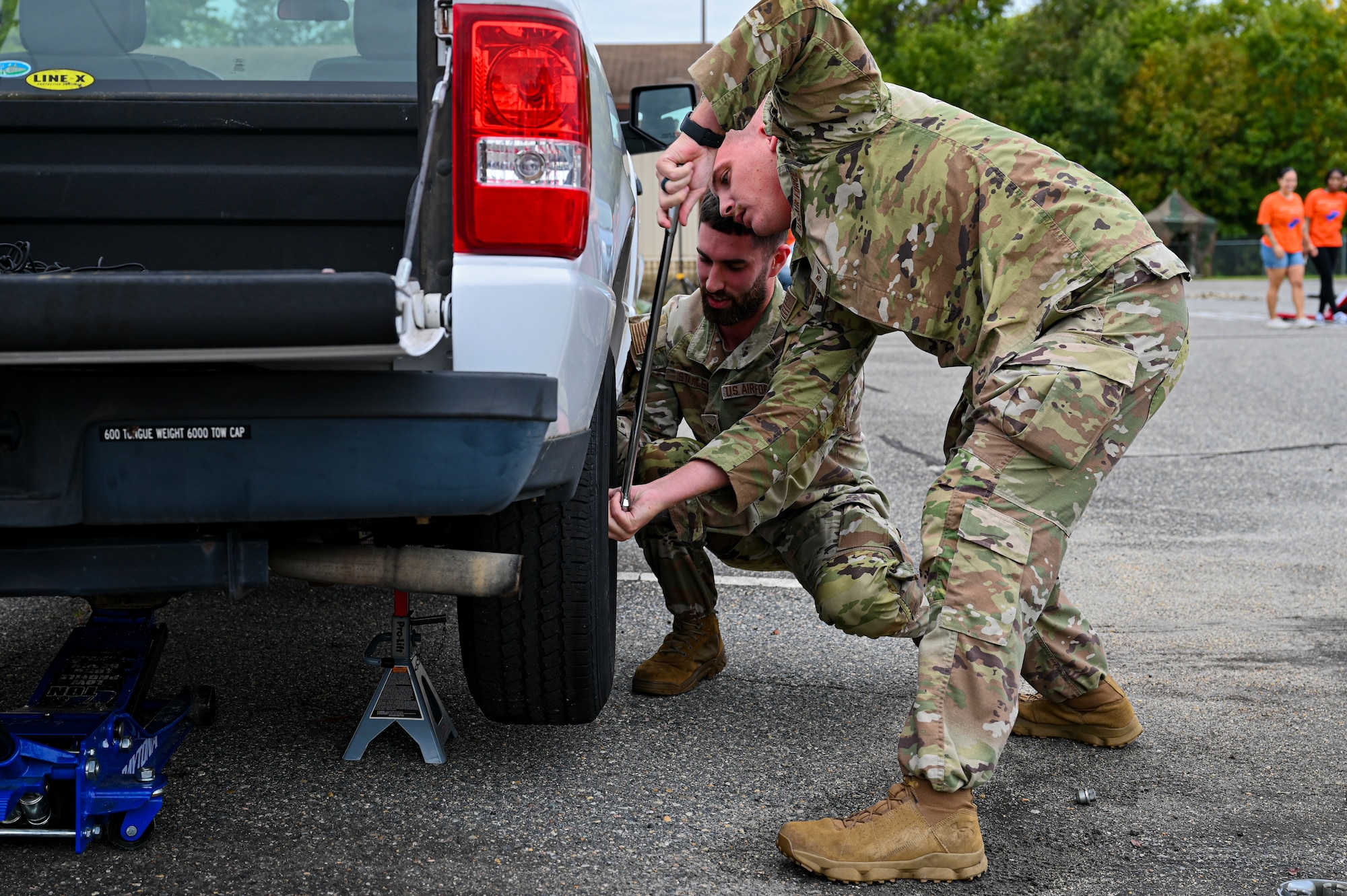 Two Airmen in uniform work together to tighten screws on a tire.