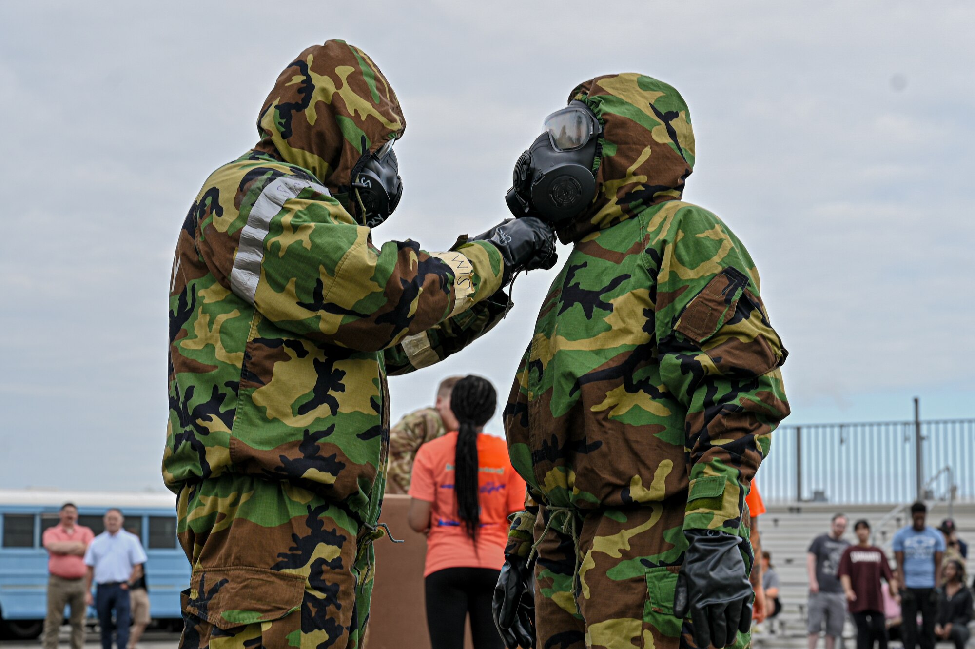 Participant on the left assists the participant to the right by using both hands to pull a tie close while putting on MOPP gear.