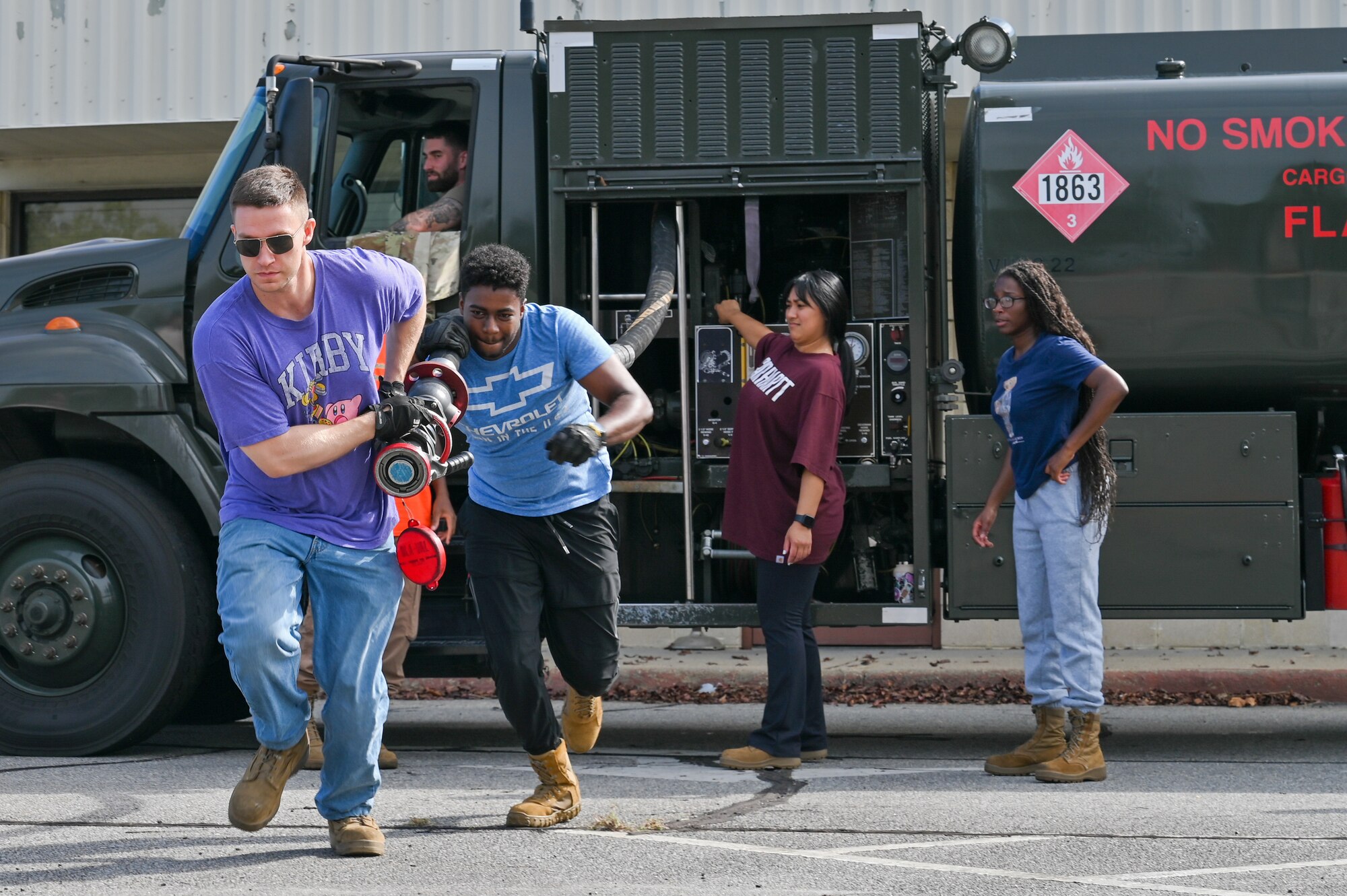 Members from LRS in civilian attire work together to run out a hose from a POL truck.