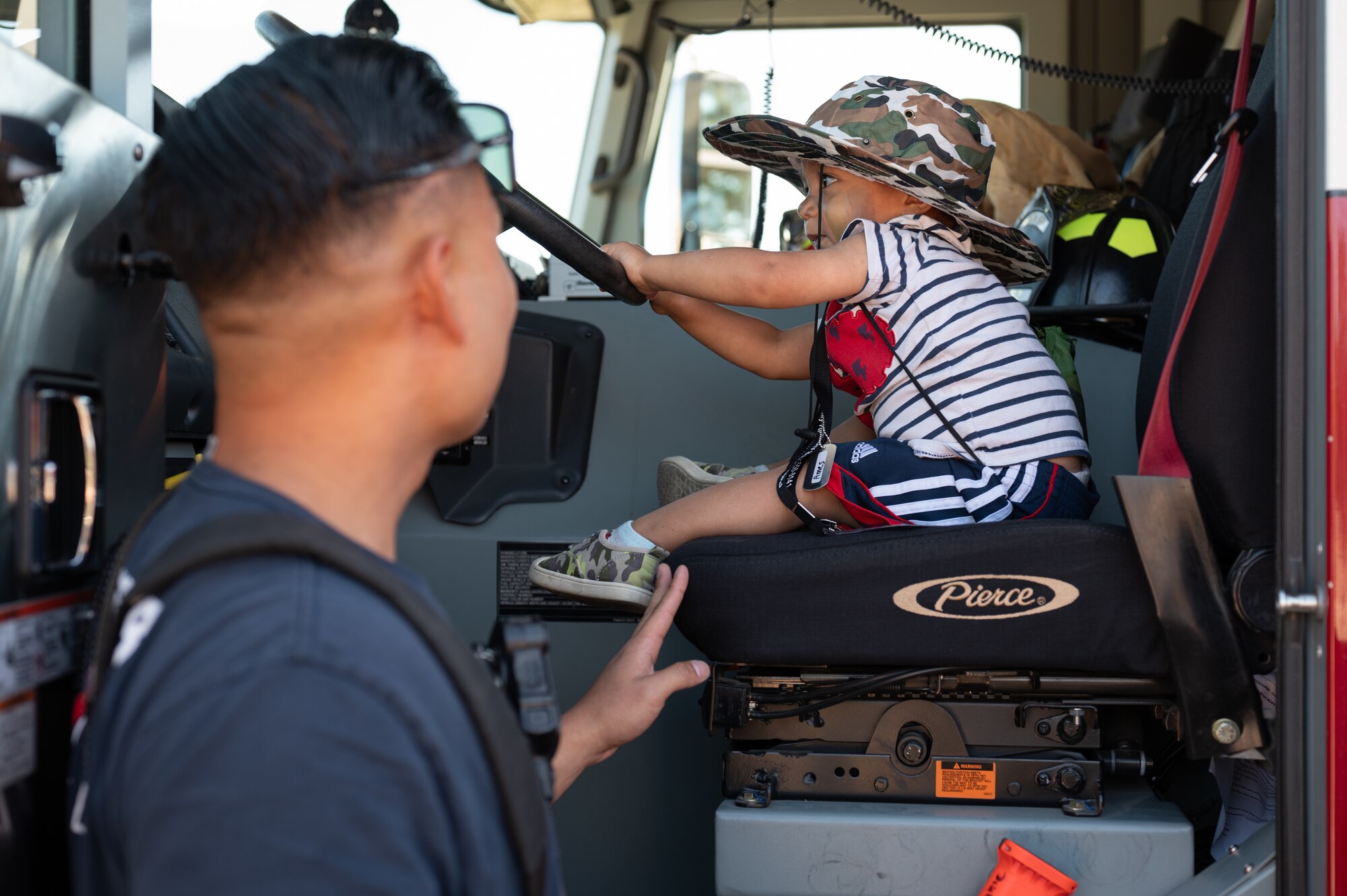A small child sits in a fire truck while a fire fighter is monitoring him.