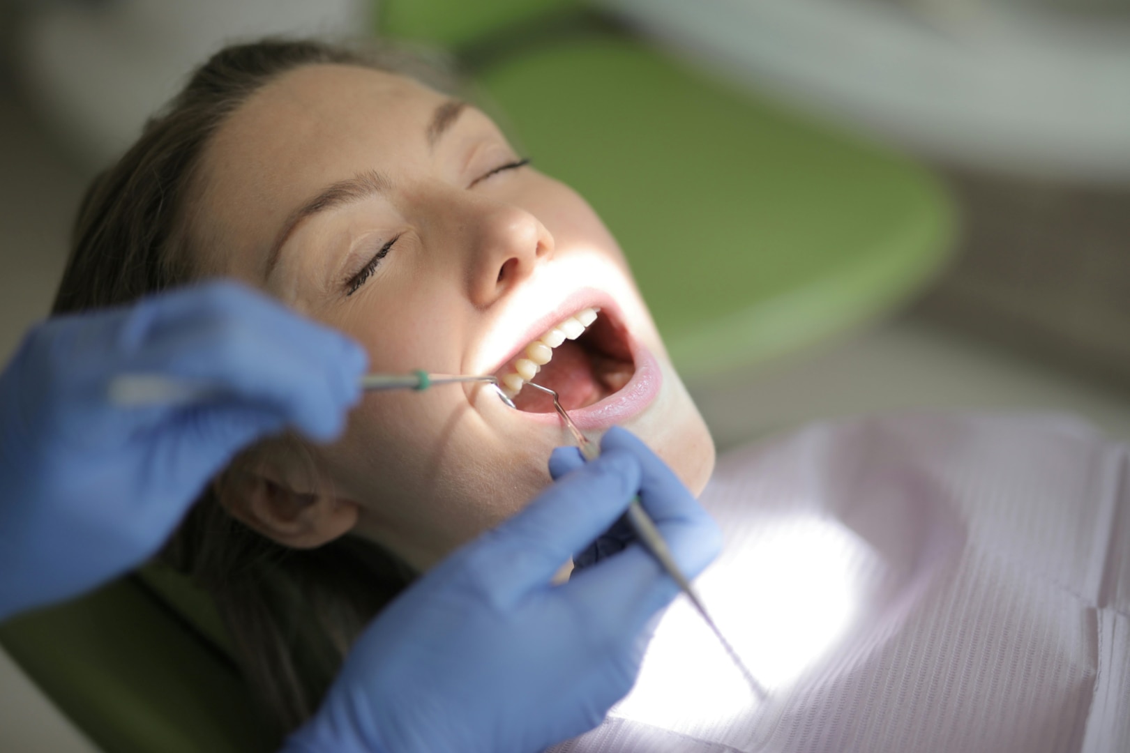 Woman lies in dental chair with eyes closed and has teeth examined.