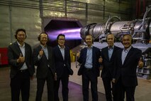 Newspapers members pose for a photo with an F-16 engine