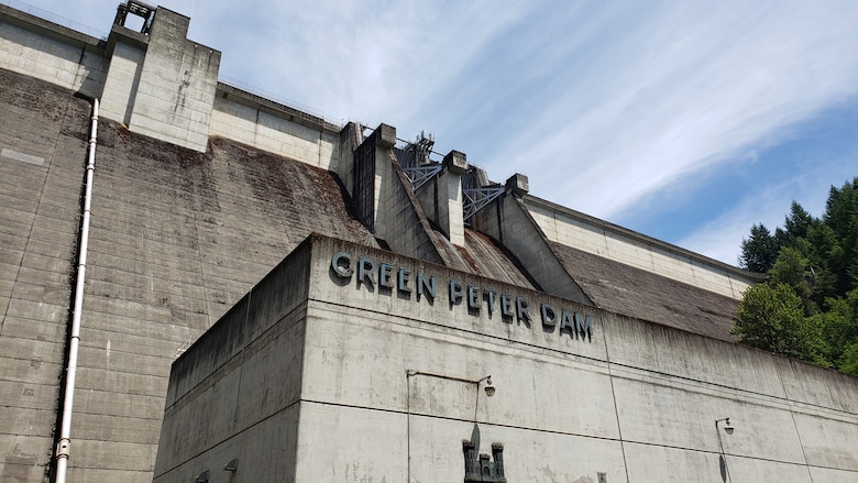 A concrete dam face with a rectangular box-like concrete building in the foreground with metal letters in the top left corner that say GREEN PETER DAM in capital letters.