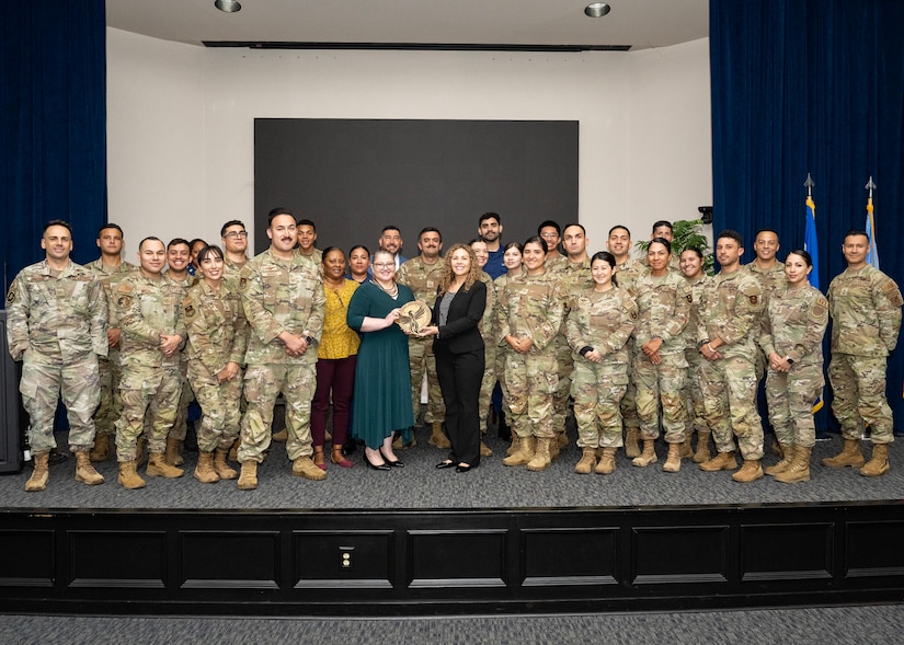 About 30 service members and a few civilians stand for a photo on a stage.