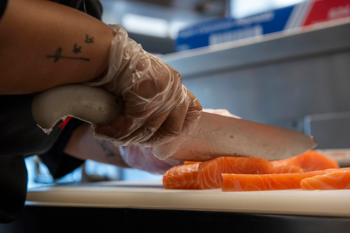close up of hand, knife and filet of fresh salmon