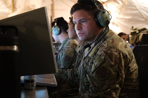 US Air Force Airmen wearing headphones work on computers