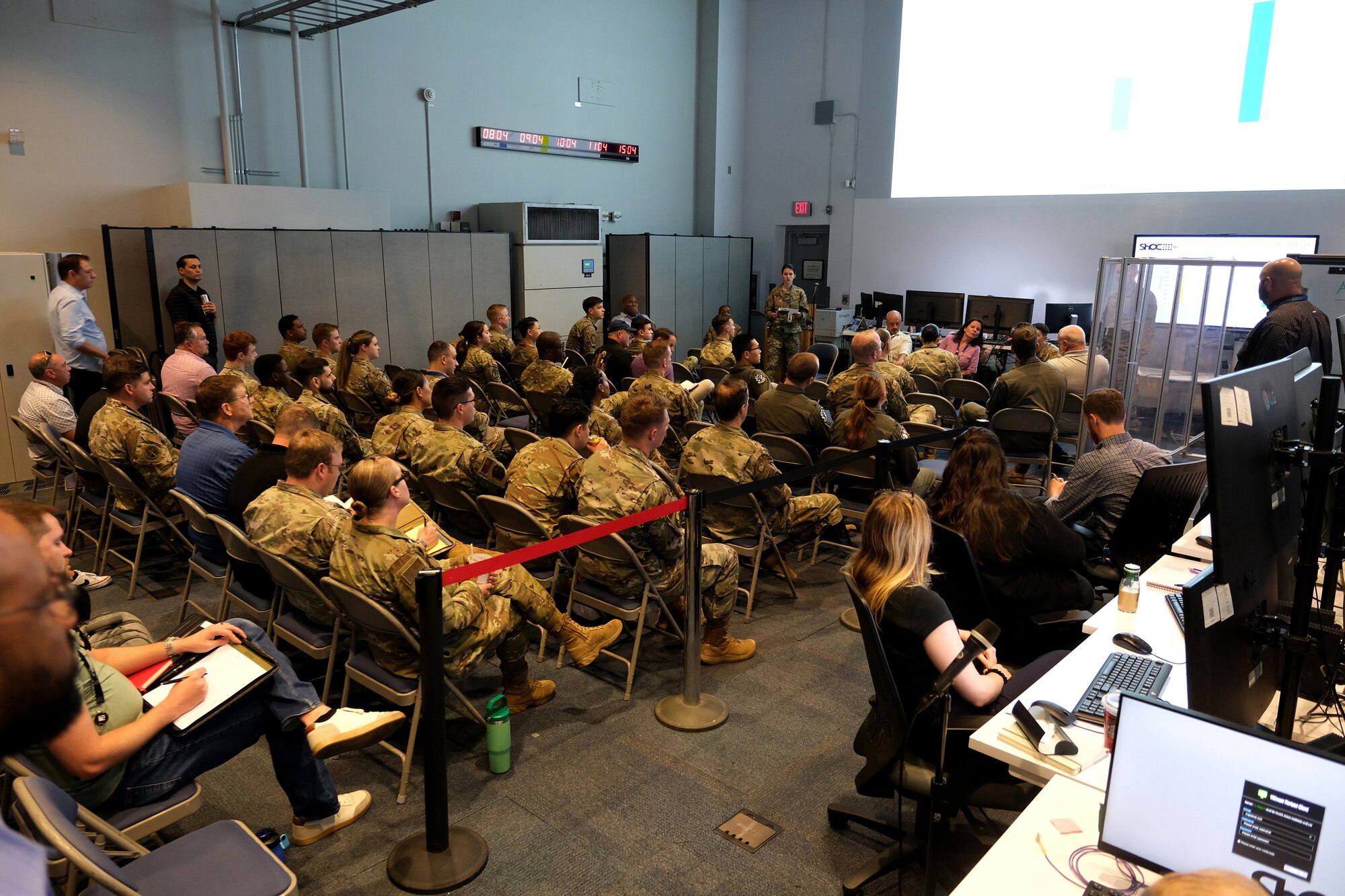photo of uniformed U.S. military and civilians sitting in chairs on an operations floor listening to a briefing