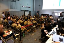 photo of uniformed U.S. military and civilians sitting in chairs on an operations floor listening to a briefing
