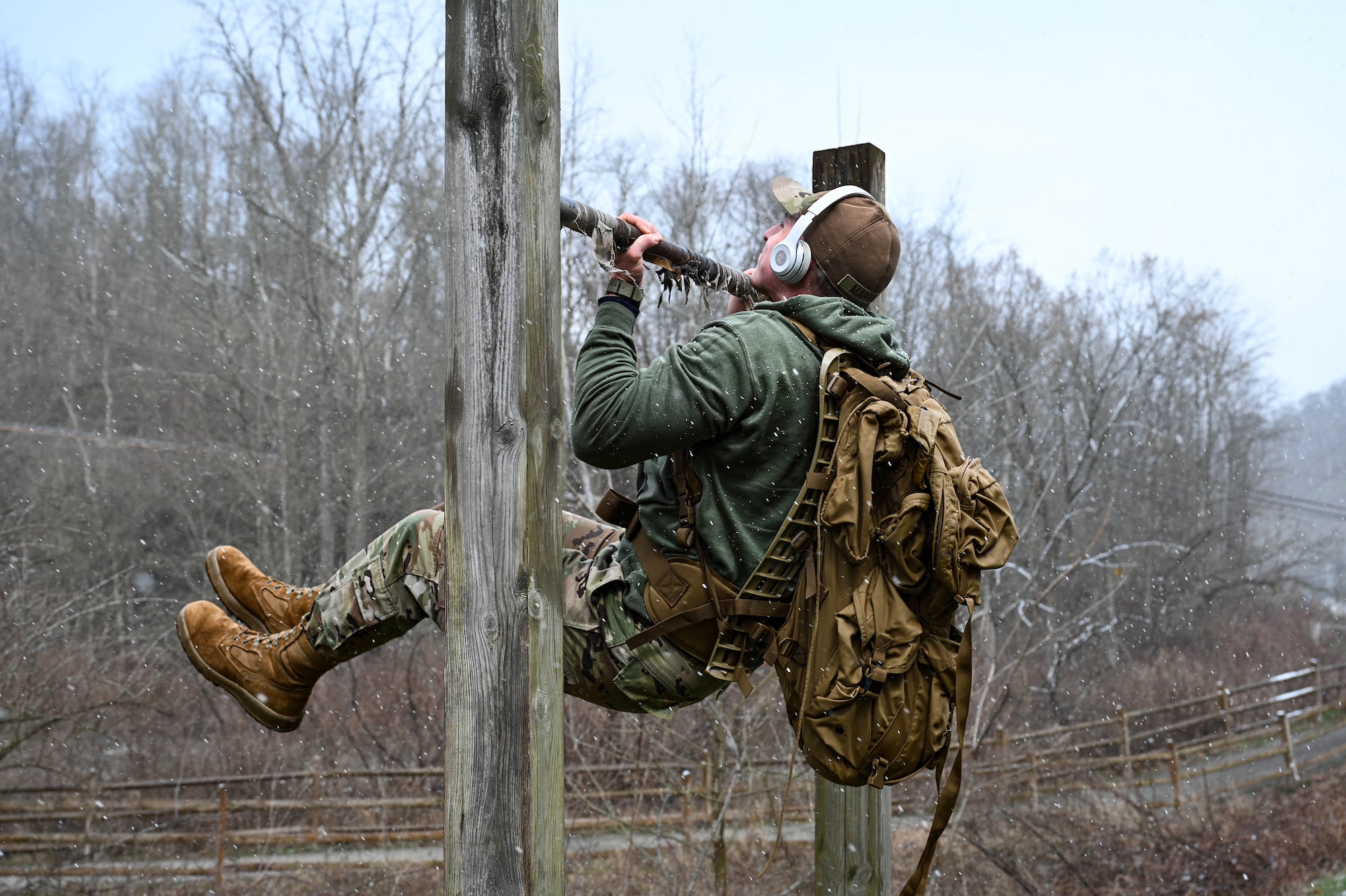 Senior Airman Martine performs underhand pullups in snowfall while wearing a collection of gear