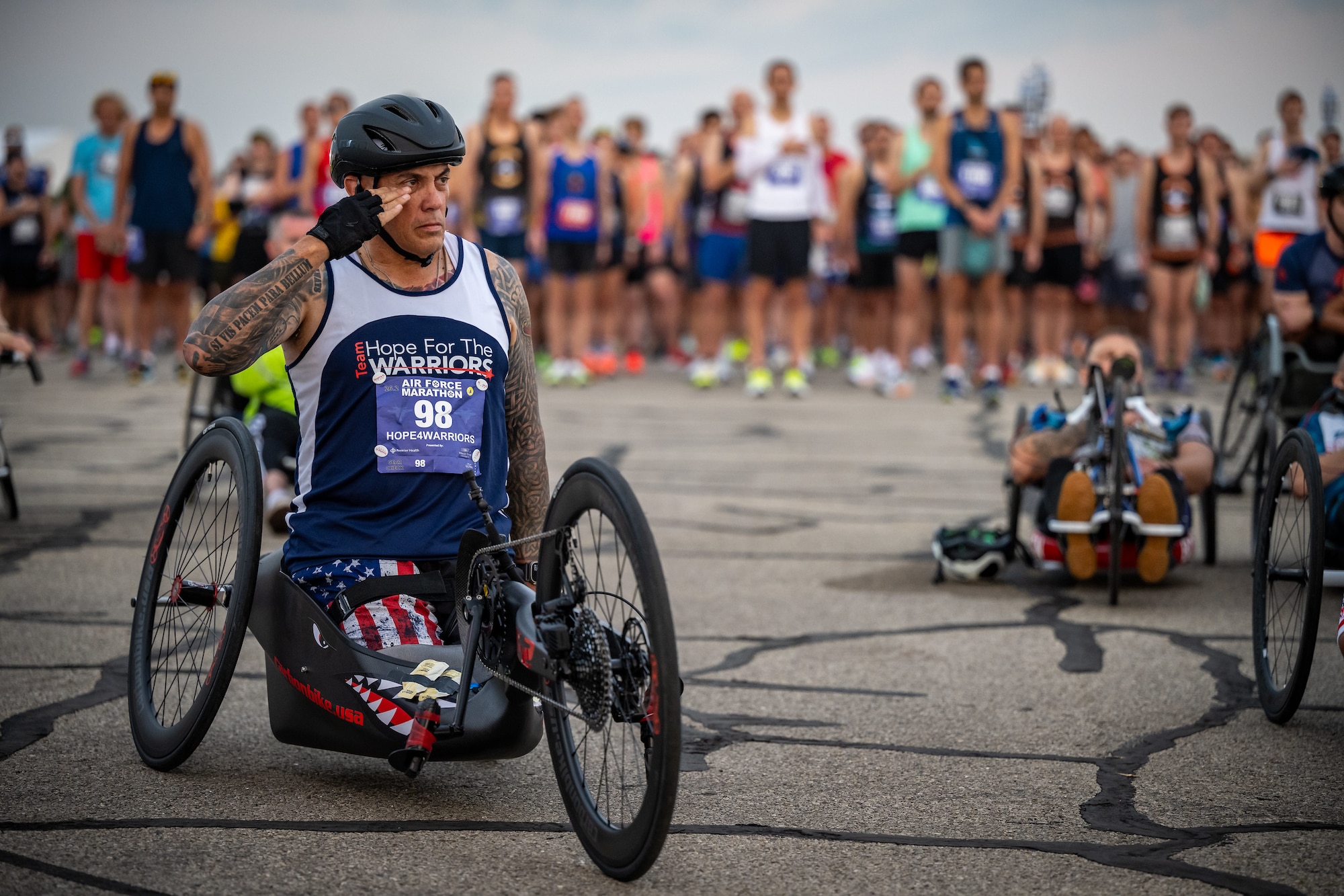 A muscular man, with heavily tattooed arms, sits tall and proud in a hand-cranked tricycle.