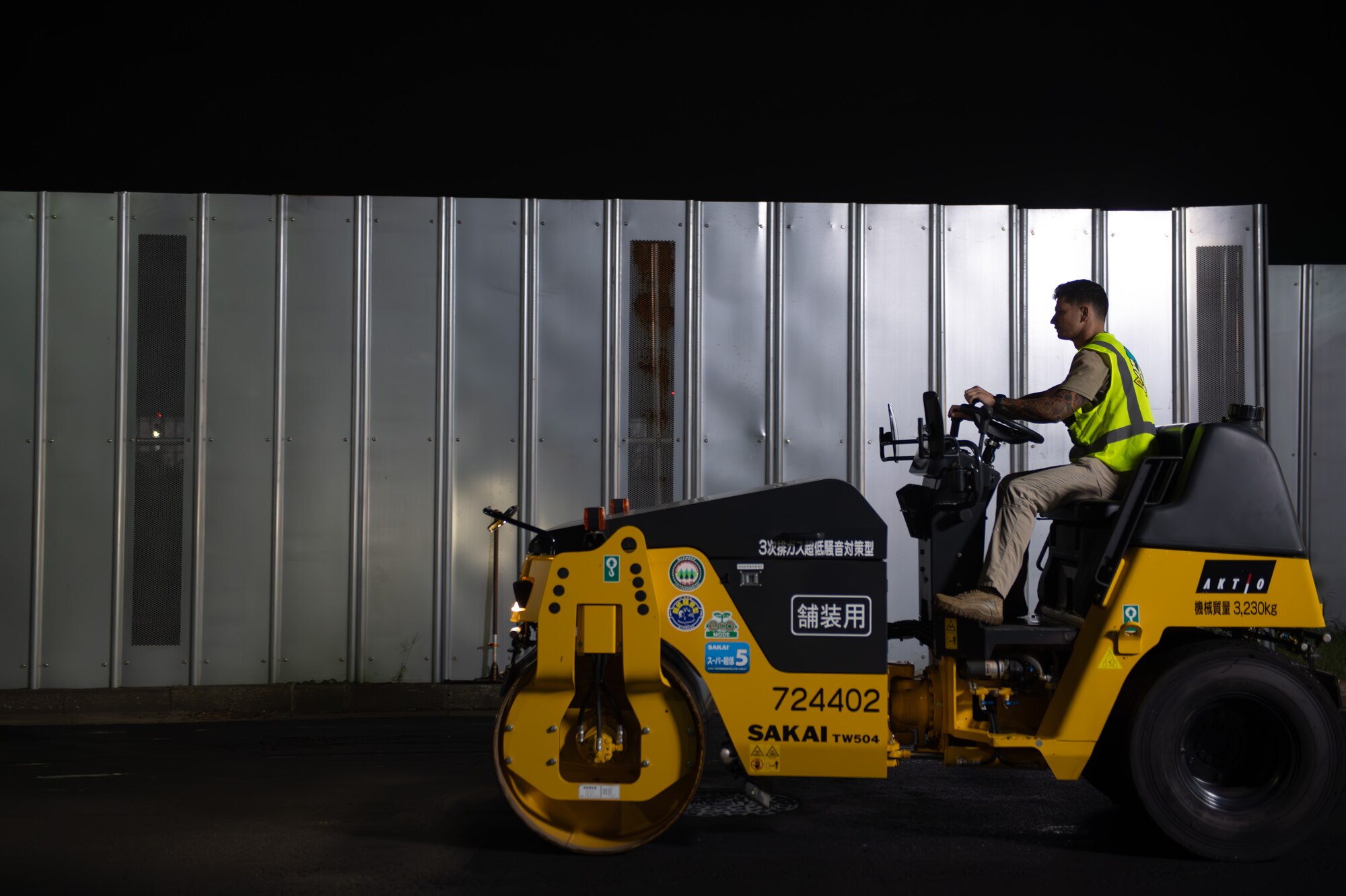 A CES member drives a drum roller to pack the freshly laid asphalt.