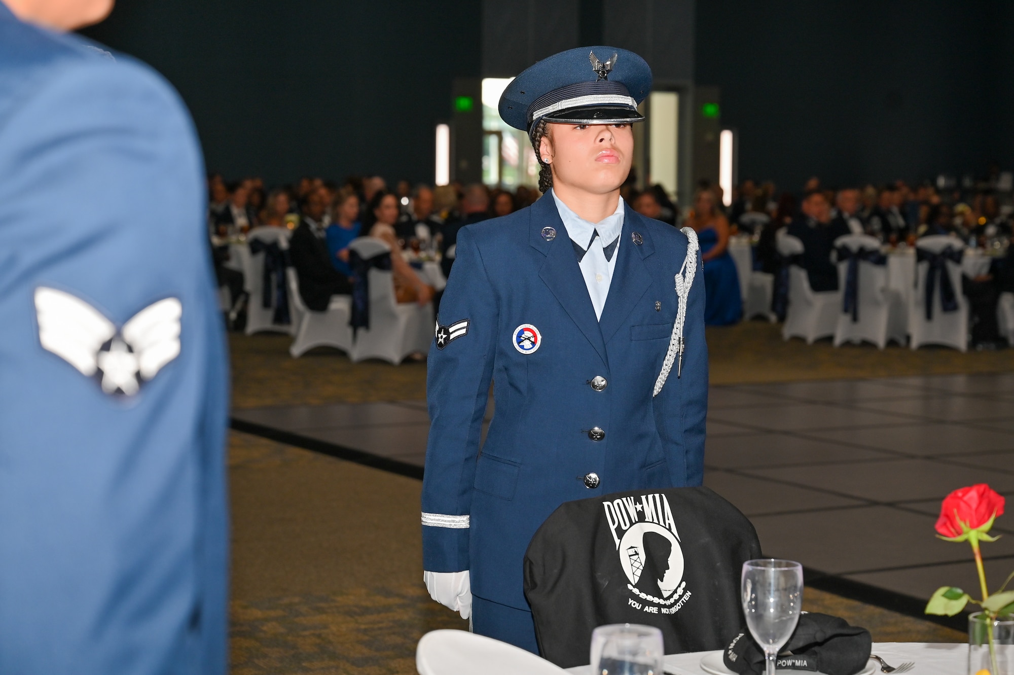 Base Honor Guard member stands at attention in front of POW/MIA table and chair.
