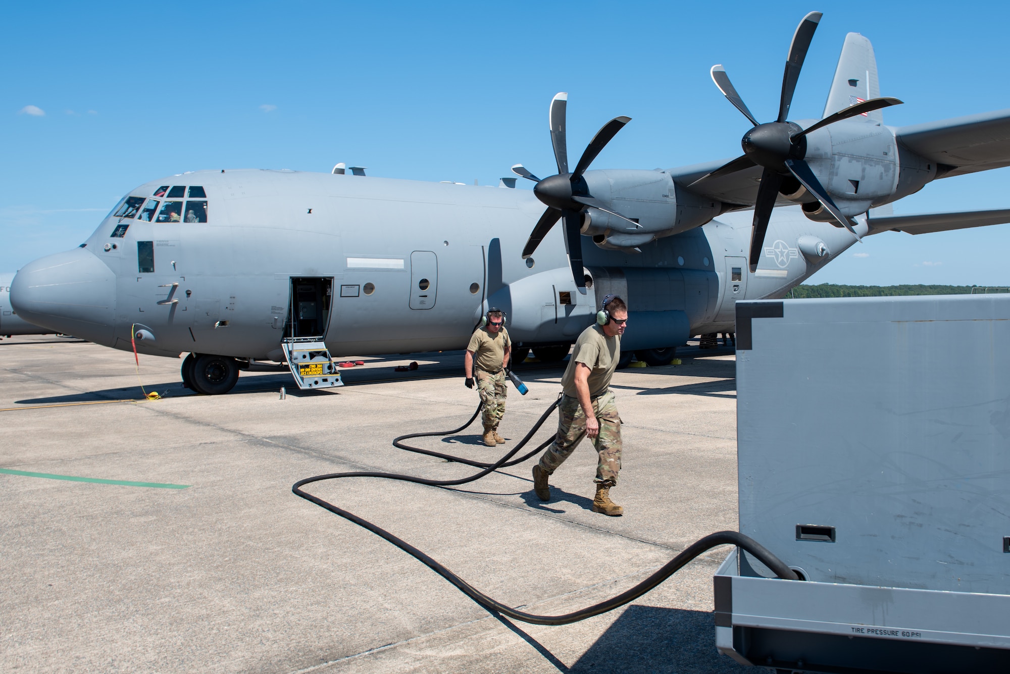 Two people carrying a fuel hose from an aircraft