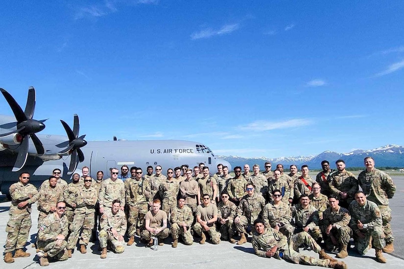 A large group of airmen pose for a photo with a military aircraft in the background.