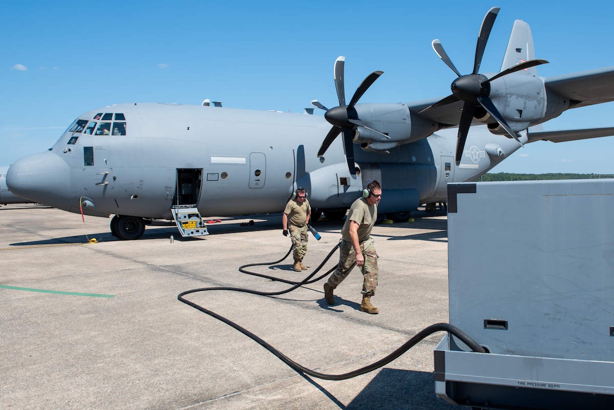 Two people carrying a fuel hose from an aircraft