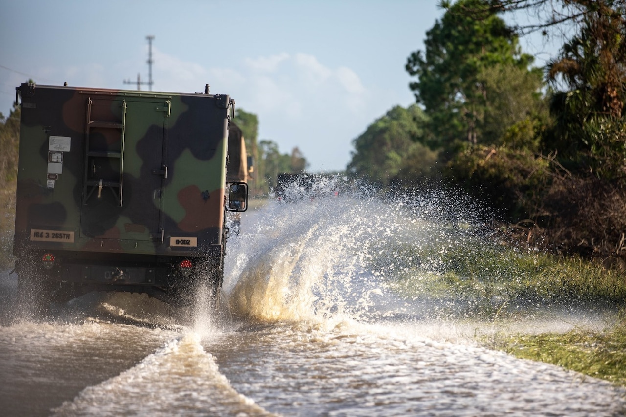 A military vehicle drives on a flooded road.