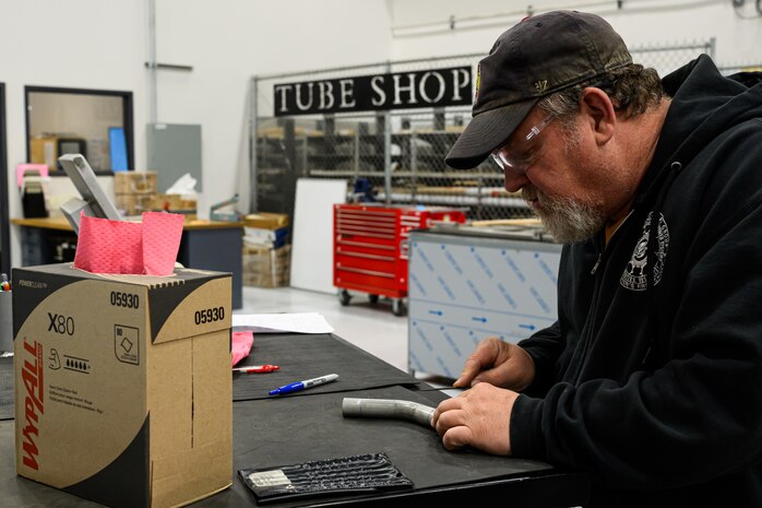 A worker uses a measuring device on a piece of pipe tubing.