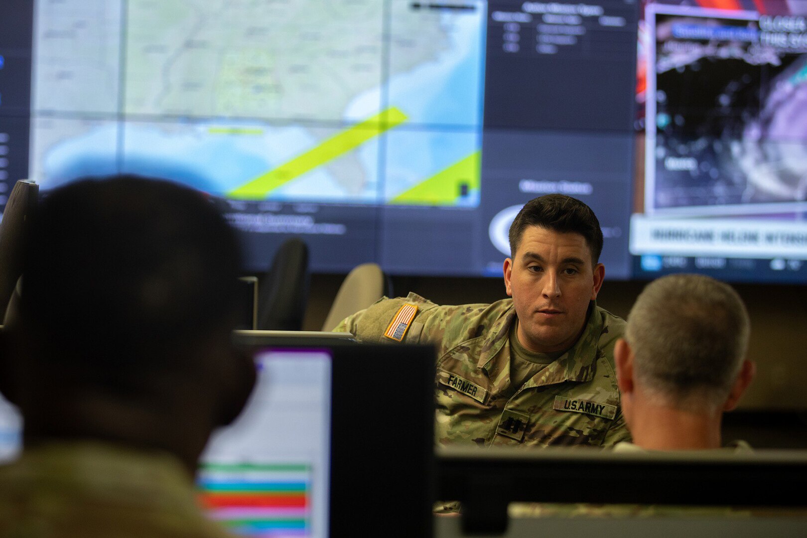 A group of guardsmen work in front of computer monitors tracking a hurricane.