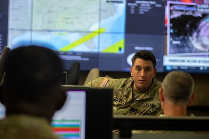 A group of guardsmen work in front of computer monitors tracking a hurricane.