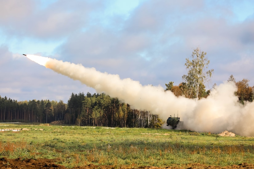 A rocket is launched from a field leaving a trail of smoke in its wake.