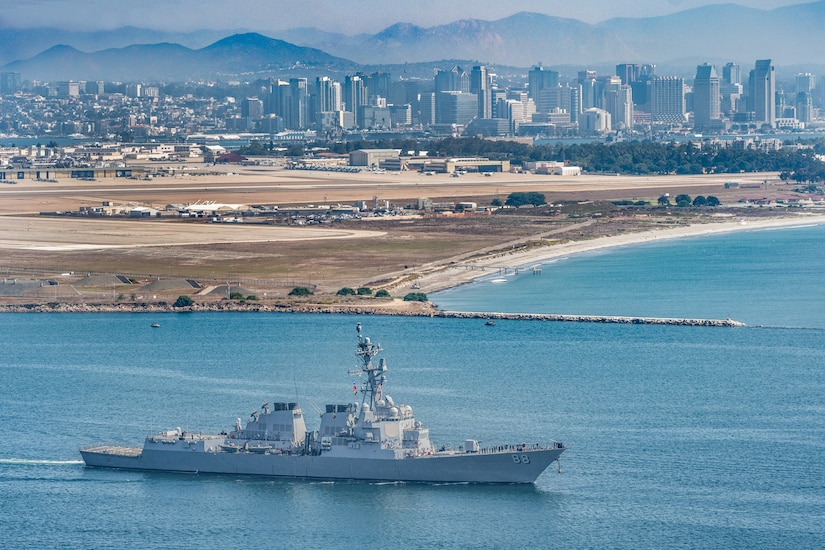 A ship sails in a body of water with a city skyline in the background.