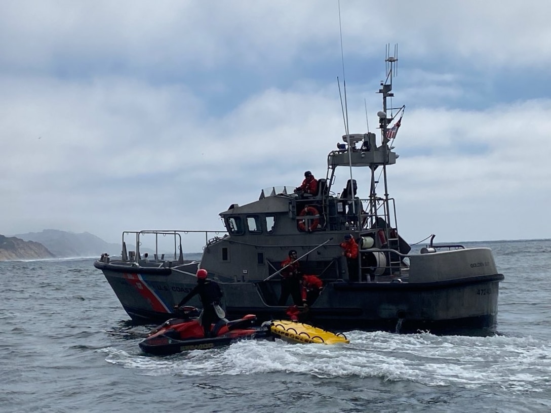 A Coast Guard 47-foot Motor Lifeboat (MLB) and its crew is seen assisting a boater off a San Francisco Fire Department jetski onto the MLB.