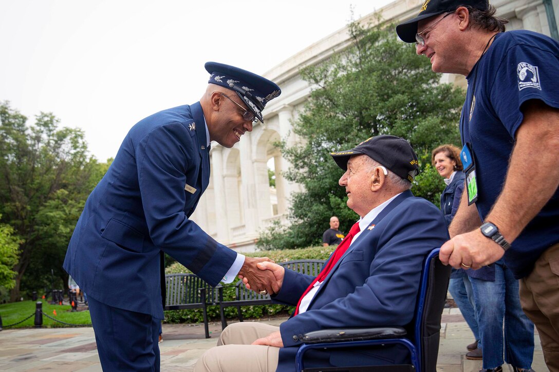 Air Force Gen. CQ Brown, Jr., shakes hands with a veteran on manicured grounds outside an ornate white structure.