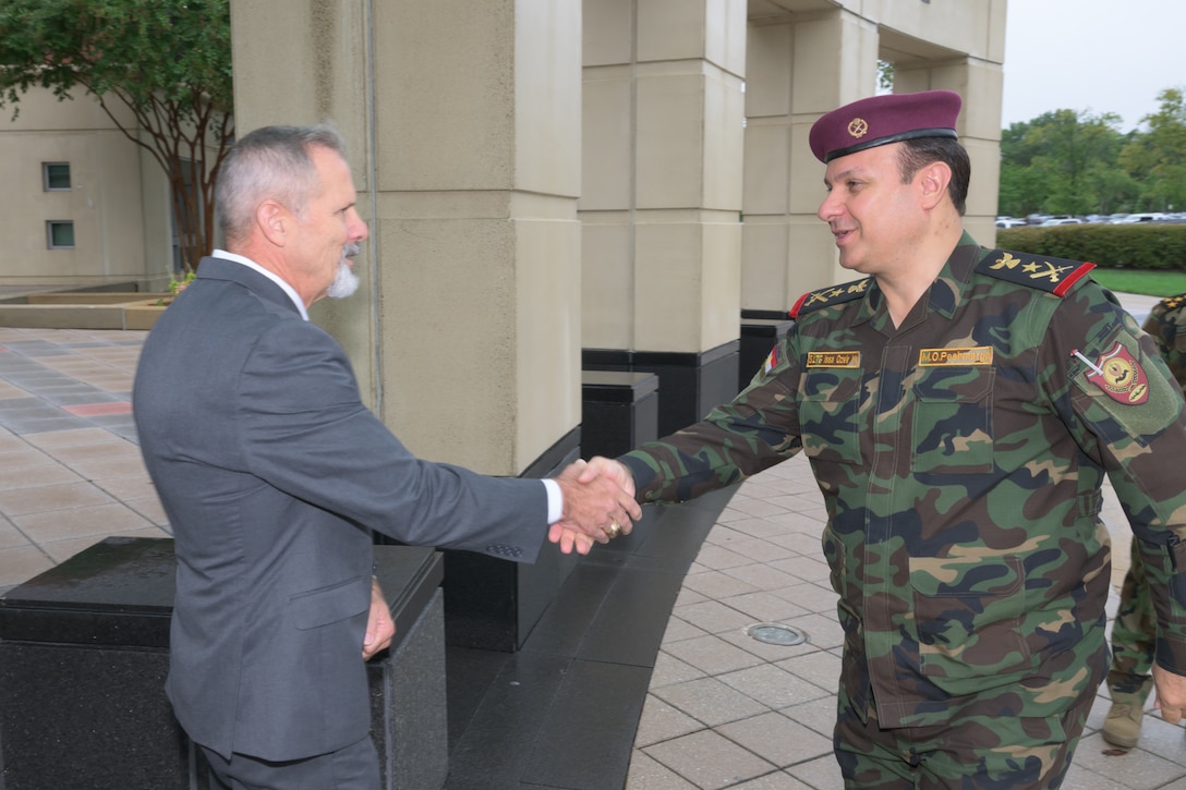Two men shake hands in front of a building.