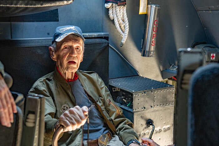A man sits inside of an aircraft crew compartment holding a cane.