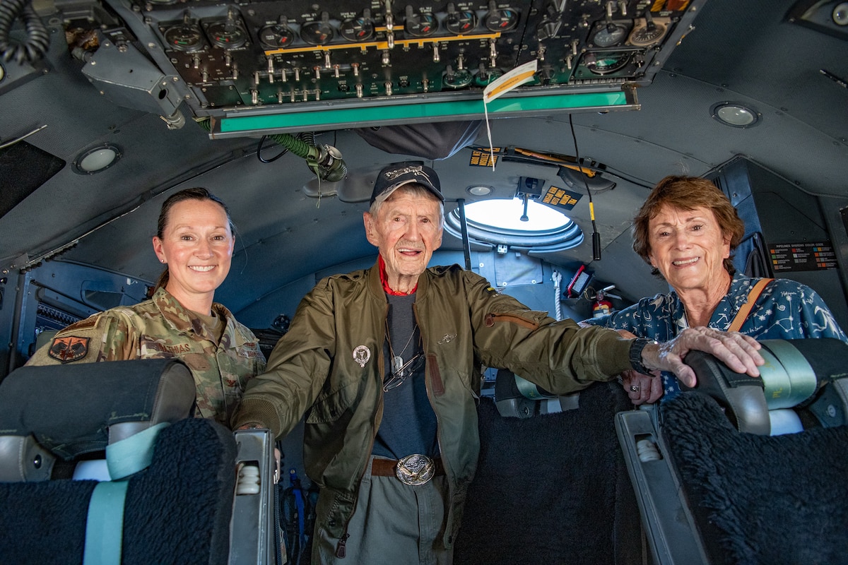 Three people stand inside of an aircraft crew compartment.