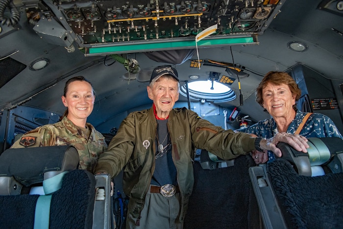 Three people stand inside of an aircraft crew compartment.