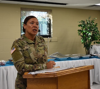 A female Army soldier in uniform speaks behind a podium.