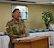 A female Army soldier in uniform speaks behind a podium.