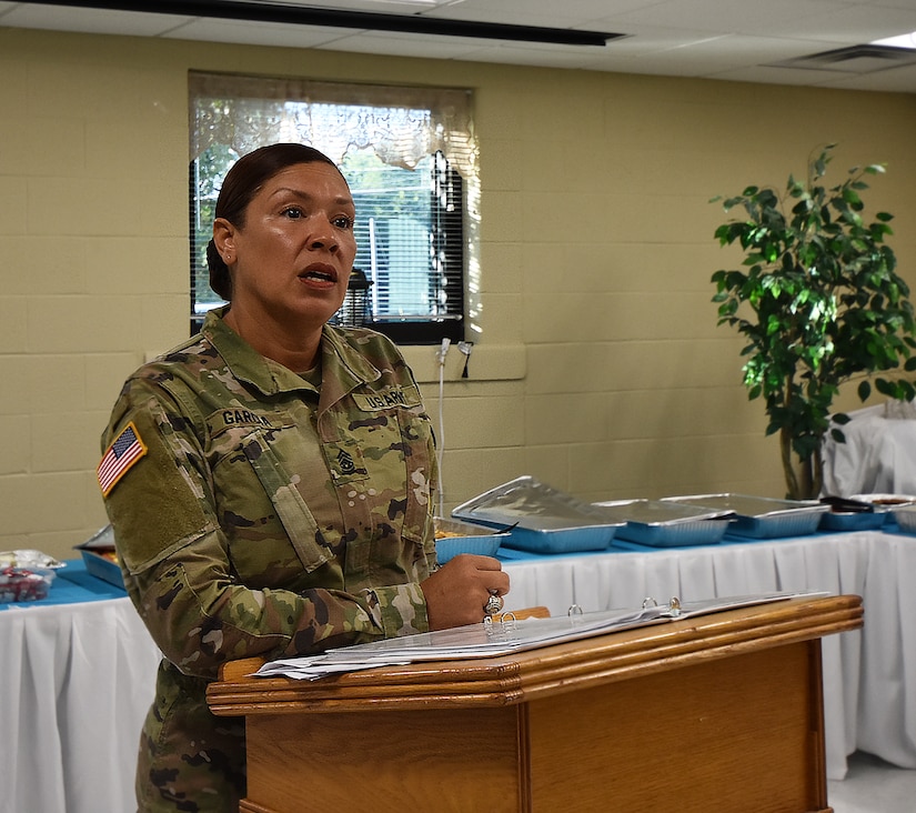 A female Army soldier in uniform speaks behind a podium.