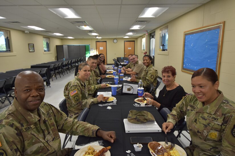 Soldiers in Army uniform and Army Civilian employees have a conversation over a pancake breakfast