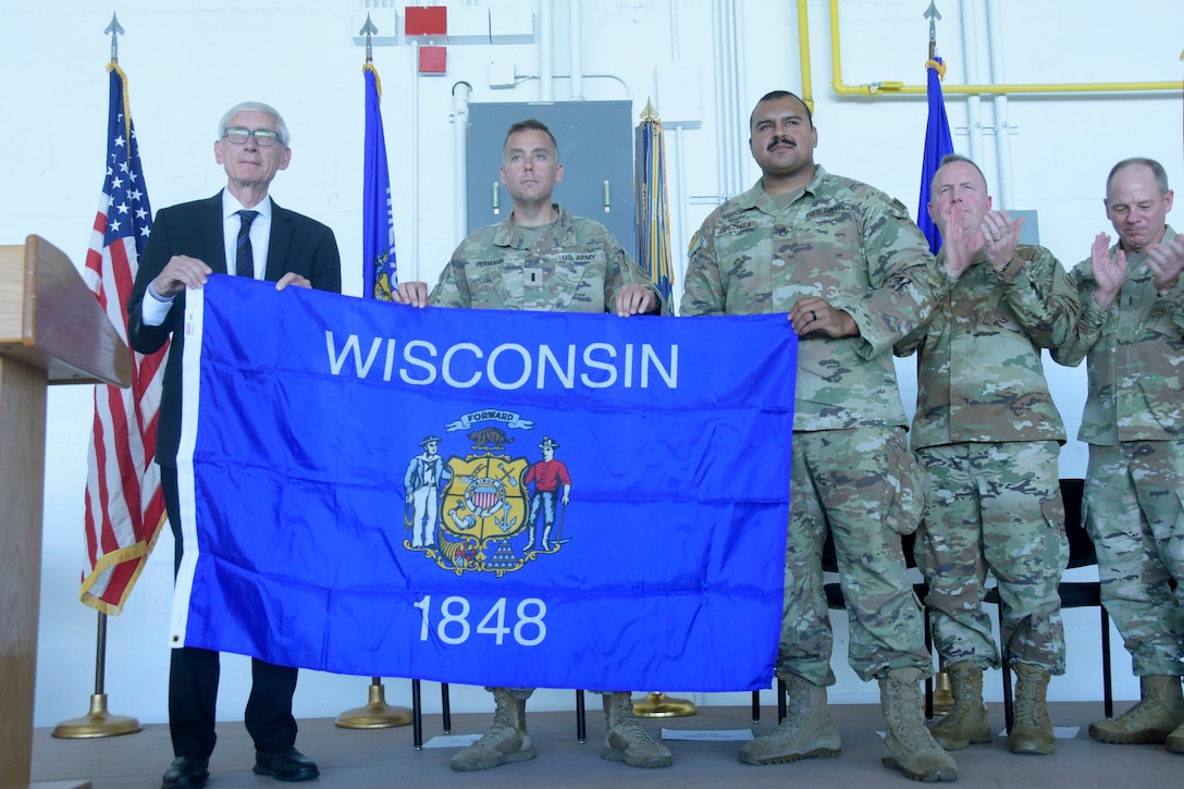 Gov. Tony Evers presents Wisconsin flags to 1st Lt. Jason Permann and Staff Sgt. Joe Perezvilla of the 457th Chemical Company, as well as the leaders of deploying units representing more than 300 Wisconsin Army National Guard Soldiers, during a formal sendoff ceremony Sept. 28 at Volk Field Air National Guard Base, Camp Douglas, Wis. The Soldiers, who are a part of the 1st Battalion, 128th Infantry Regiment, the 1st Battalion, 120th Field Artillery Regiment, the 132nd Brigade Support Battalion and the 457th Chemical Company, will be deploying to both U.S. Central Command in Southwest Asia and U.S. Africa Command, Horn of Africa. The deploying Soldiers will support ongoing operations through tactical missions, and provide medical care capabilities across the region. Wisconsin Department of Military Affairs photo by Vaughn R. Larson