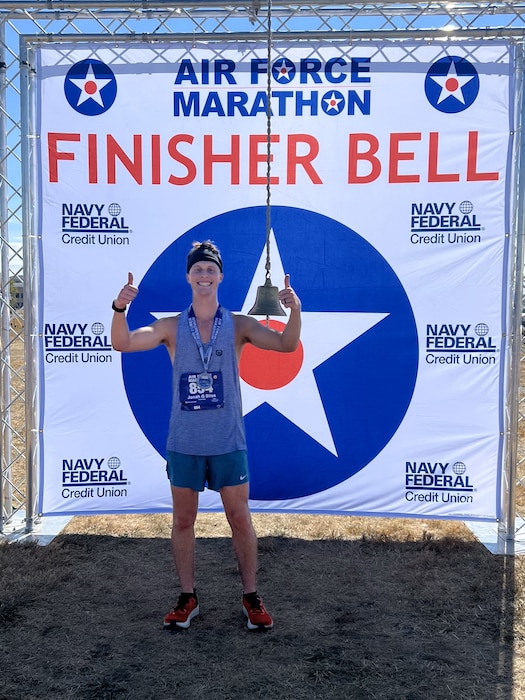 U.S. Air Force Airman 1st Class Jonah Bliss, 97th Air Mobility Wing public affairs apprentice, smiles for a photo in front of the 2024 Air Force Marathon finisher bell at Wright-Patterson Air Force Base, Ohio, Sept. 21, 2024. Finishing the marathon taught Bliss a lesson on how to overcome life’s challenging obstacles. (Courtesy photo)