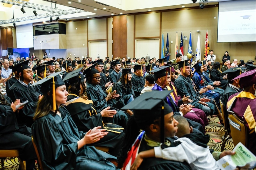 Young people in caps and gowns are seated in an auditorium.