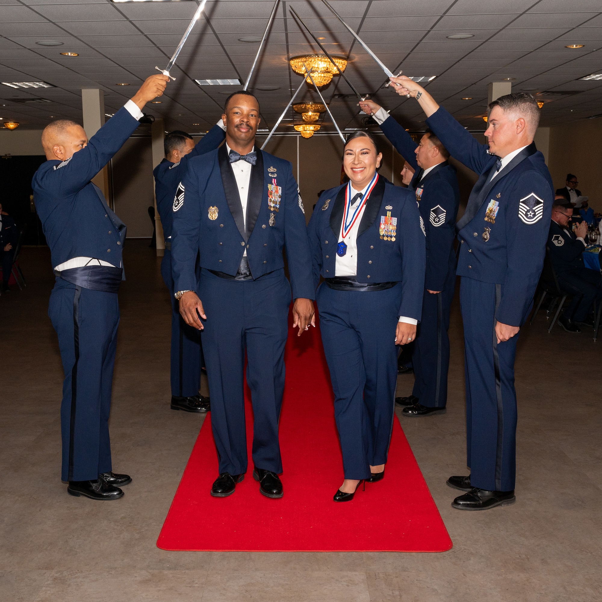 U.S. Air Force (M)Sgt Emily Morris, 47th Security Forces Squadron, walks under the Saber Team's swords during the senior non-commissioned officer induction ceremony at Laughlin Air Force Base, Texas, Sept. 27, 2024. The induction ceremony brings Airmen together to celebrate the achievement of entering the realm of senior enlisted leaders. (U.S. Air Force photo by Staff Sgt. Nicholas Larsen)
