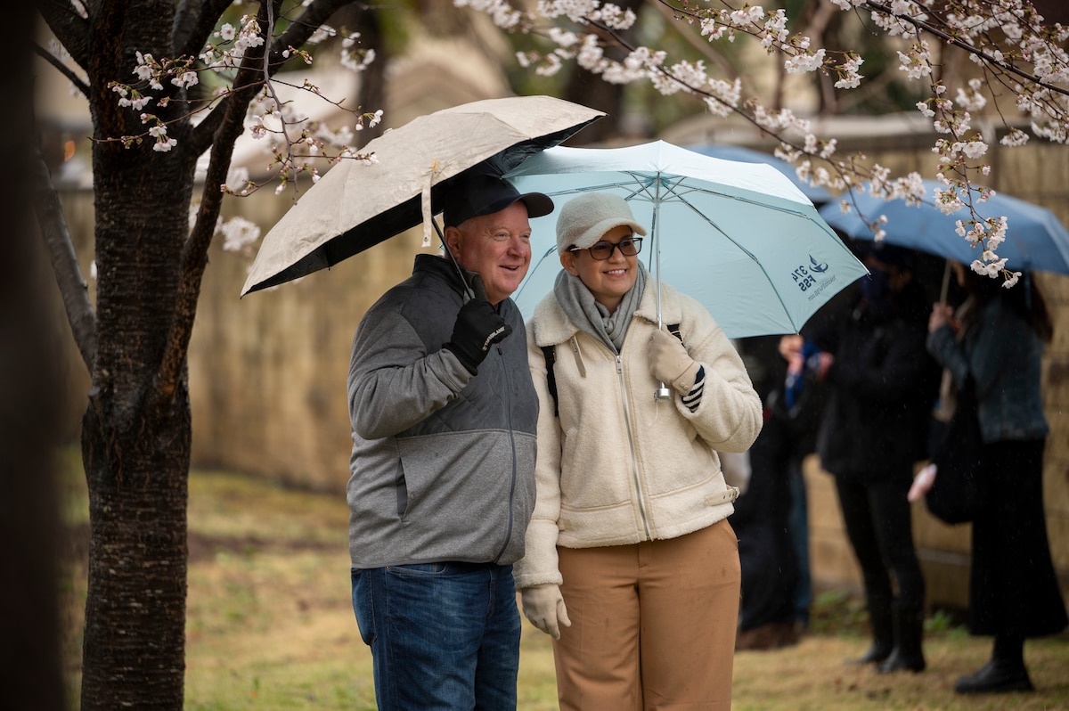 A couple poses for a photo in front of a sakura tree.
