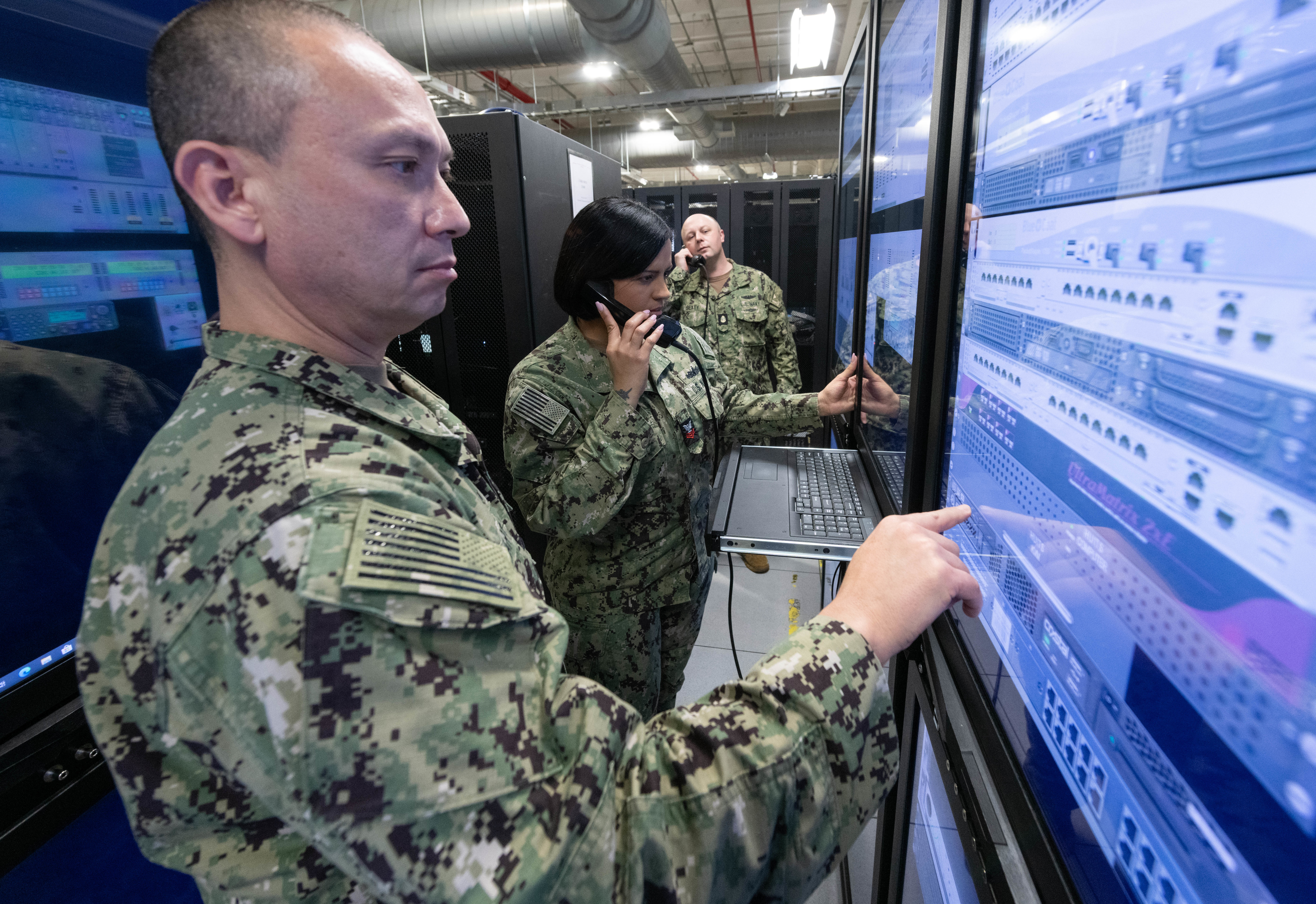 People in uniform examining and adjusting electronic panels.